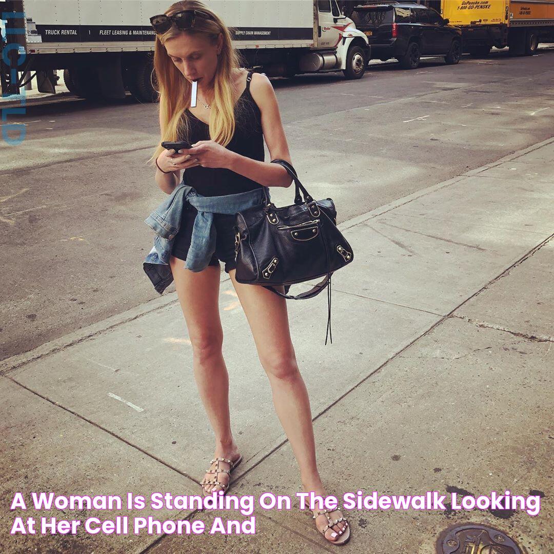 a woman is standing on the sidewalk looking at her cell phone and